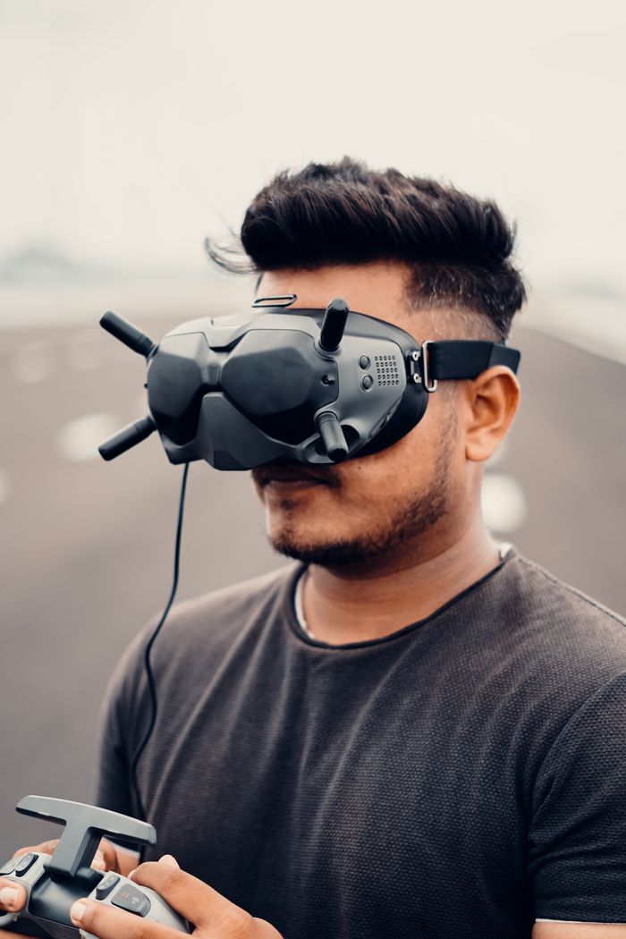 services-01 Young man using drone goggles and controller for immersive outdoor experience.
