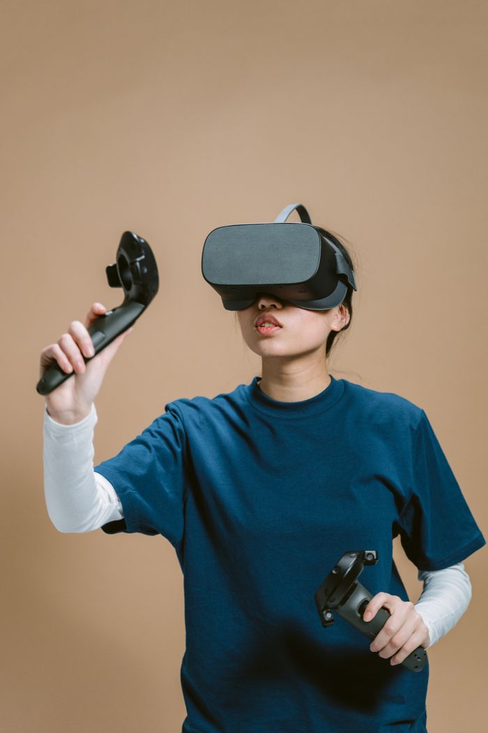 services-02 Young woman wearing VR headset and using controllers for an immersive virtual reality experience on a beige background.